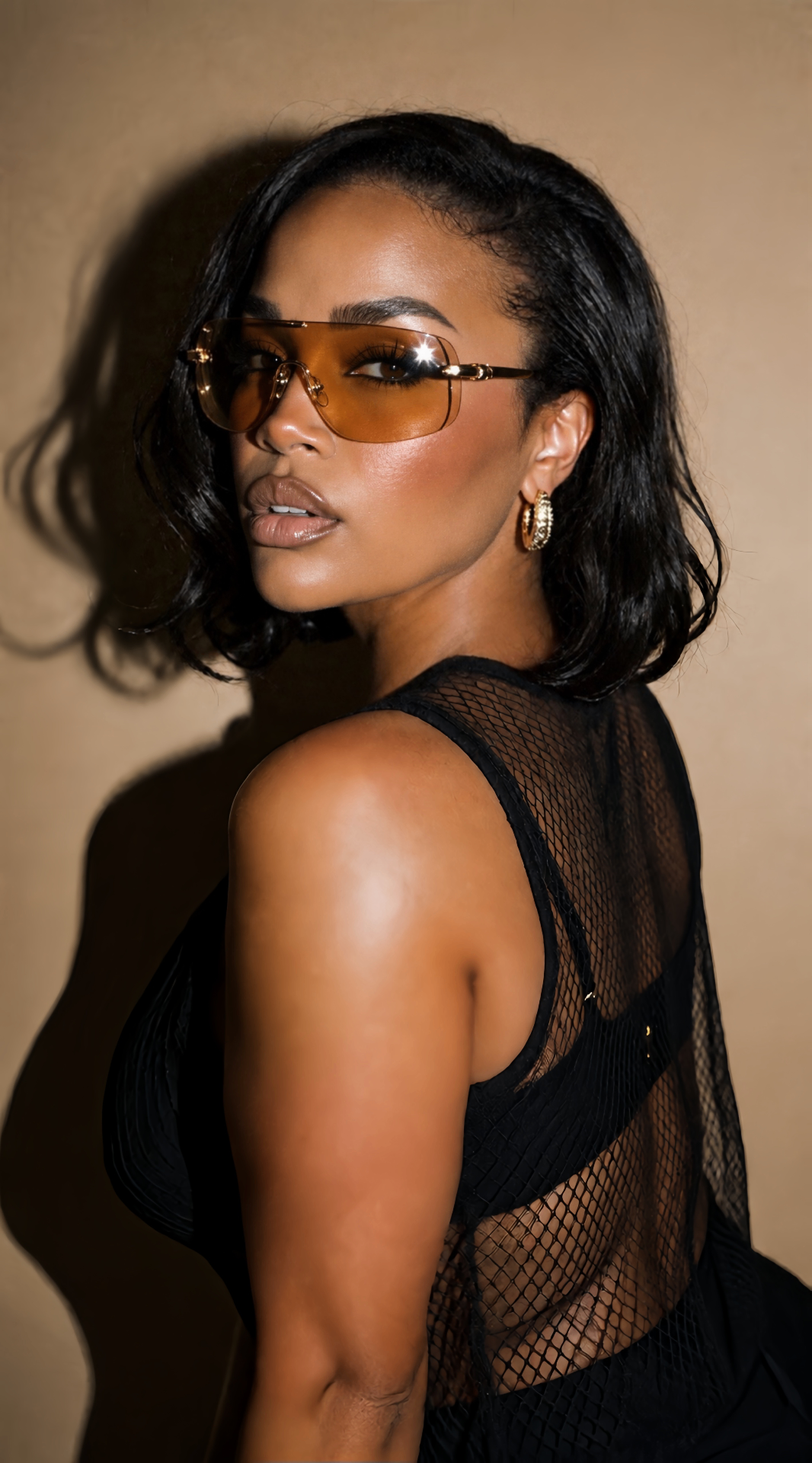 NiCalé photographed with direct flash in amber sunglasses, gold hoops and a black mesh top